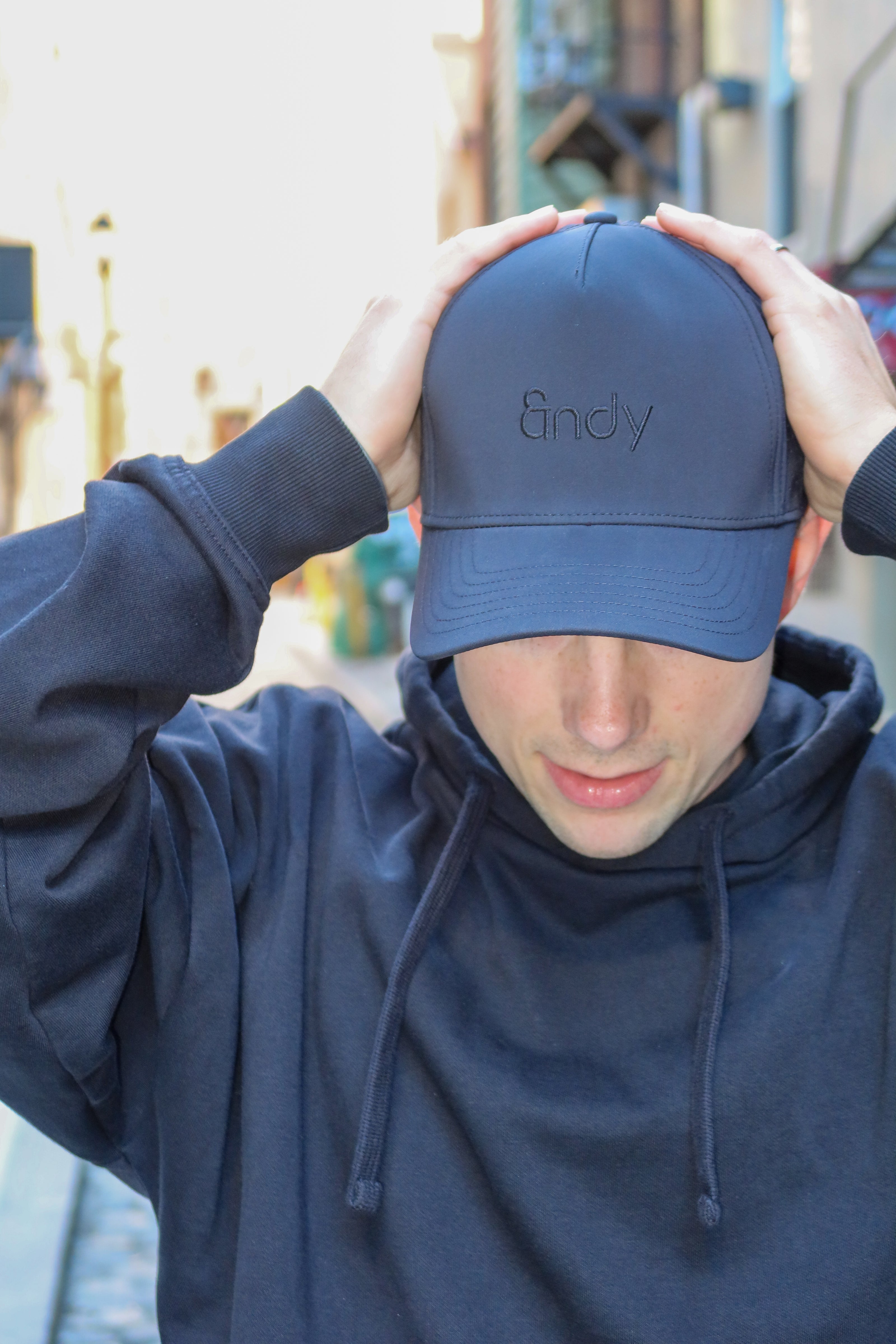 Person wearing a navy blue cap with 'Andy' branding, holding it above their head.