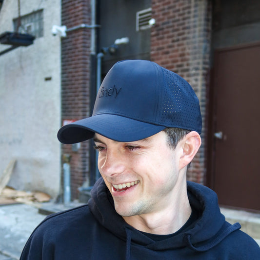 Man wearing a black cap and hoodie outdoors with a brick building in the background