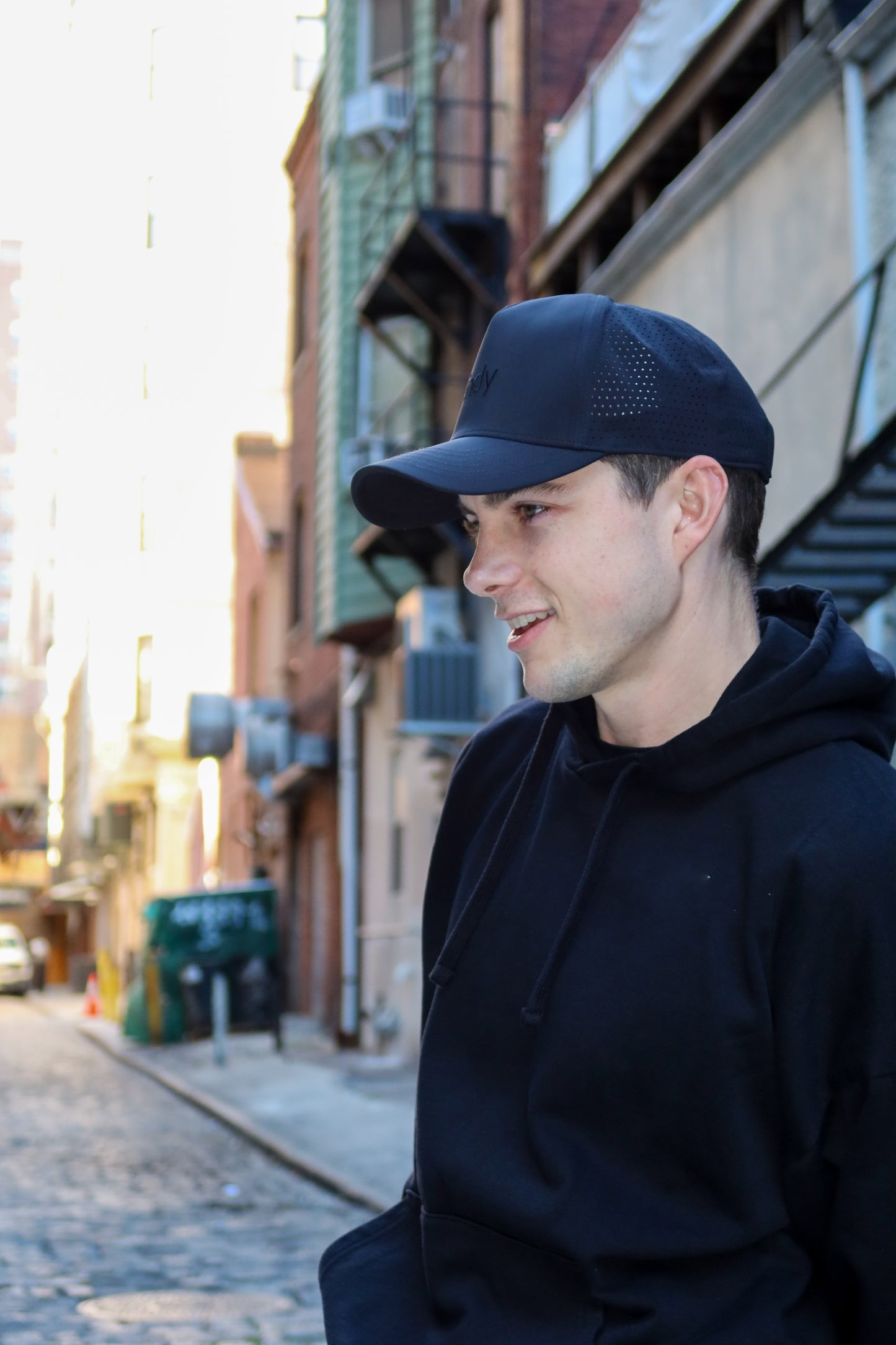 Man wearing a black cap and hoodie standing on a street with buildings in the background