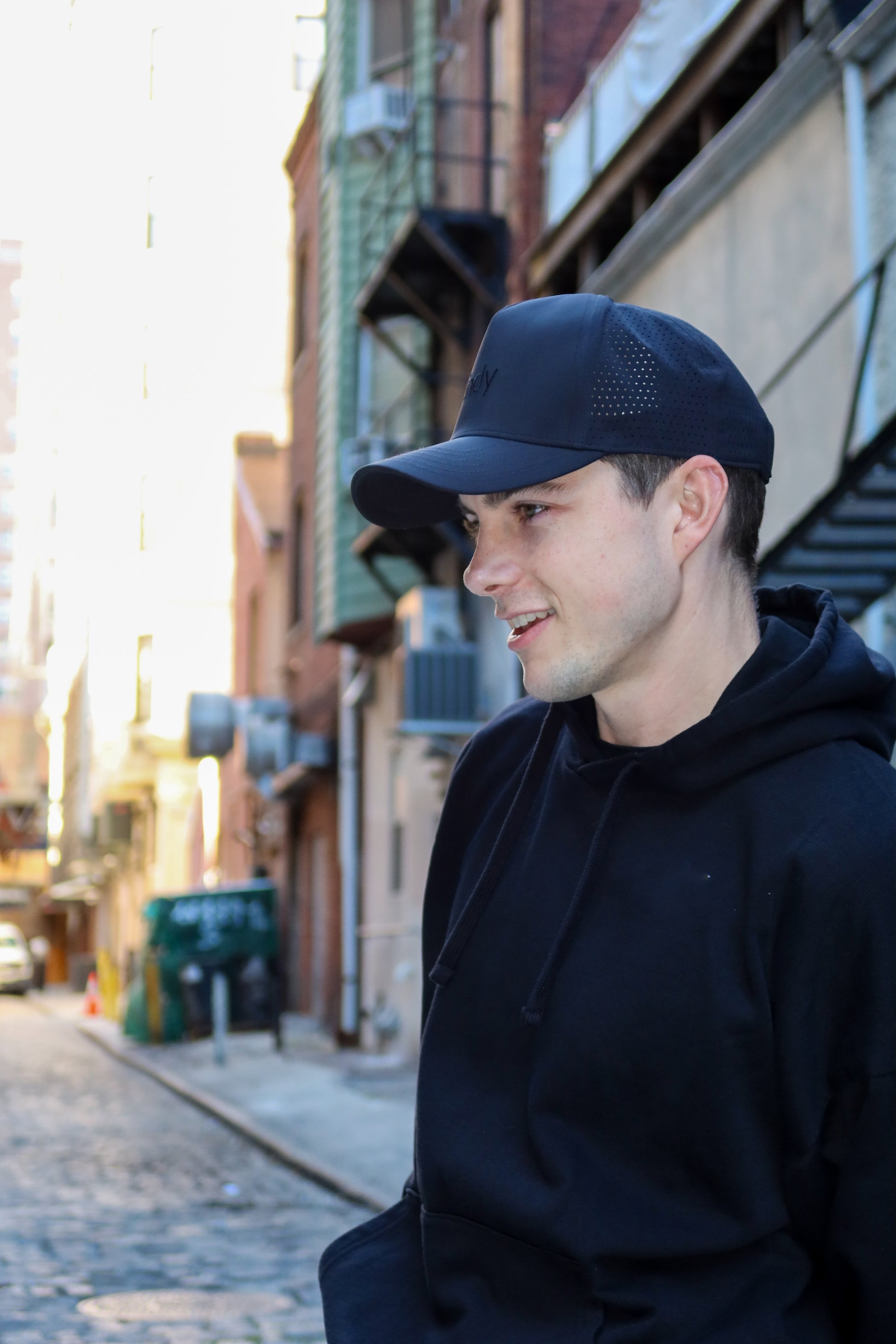 Man wearing a black cap and hoodie standing on a street with buildings in the background