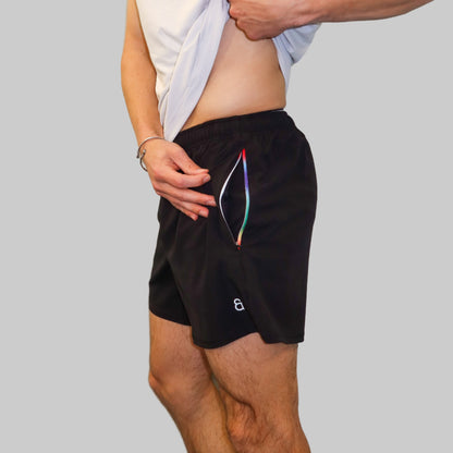 Person wearing a white tank top and black shorts with a colorful drawstring, standing against a light blue wall.