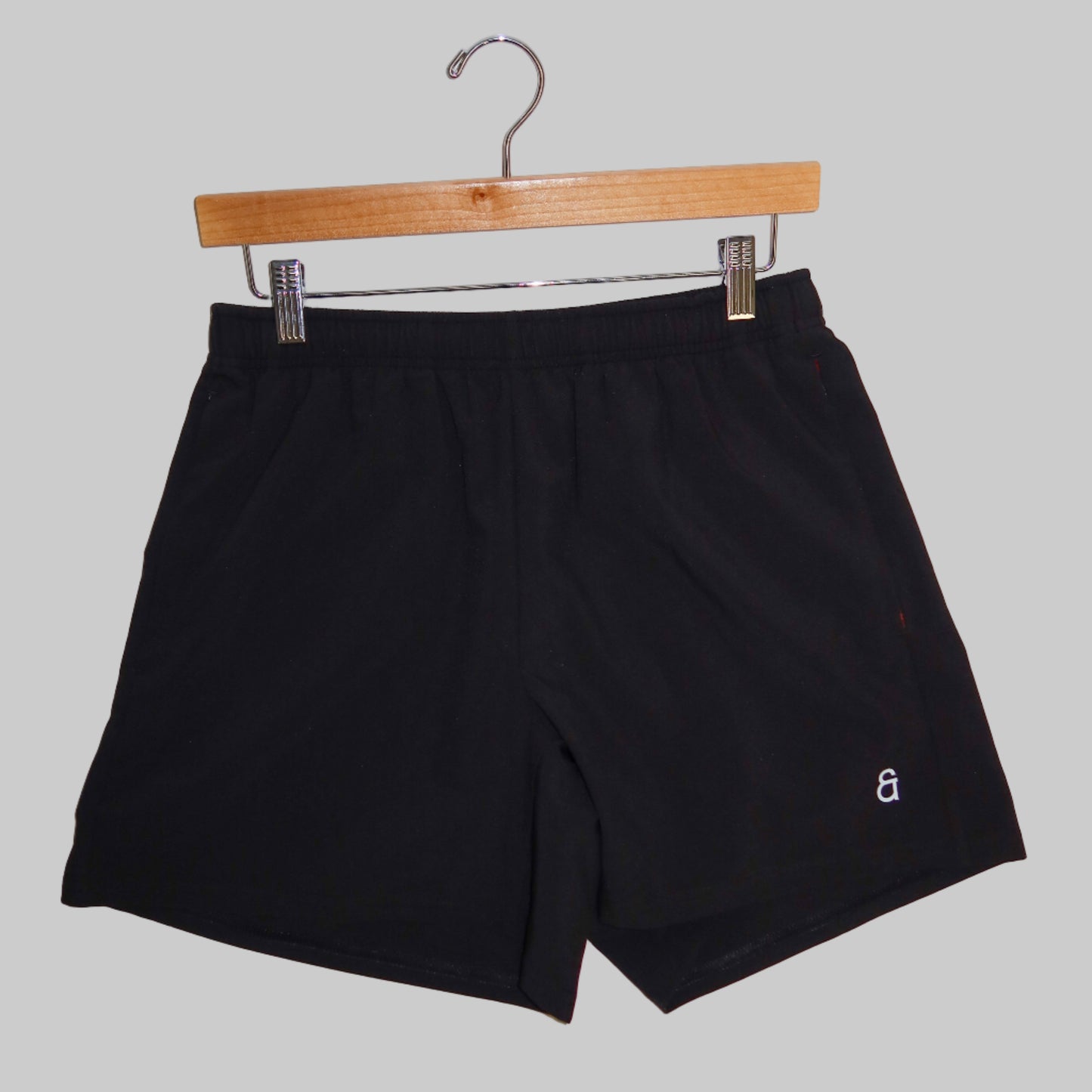Black shorts on a wooden hanger against a white background