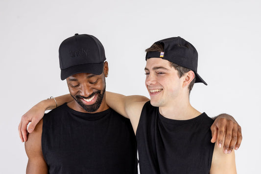 Two men wearing black caps and sleeveless shirts standing close together on a plain background