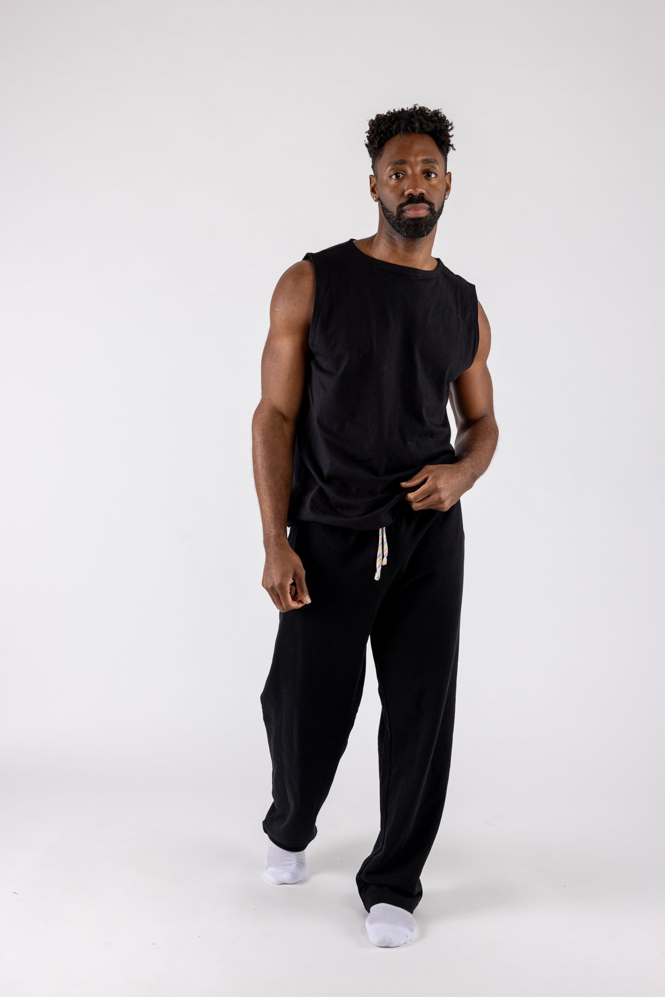 Man wearing a black sleeveless shirt and black pants on a white background