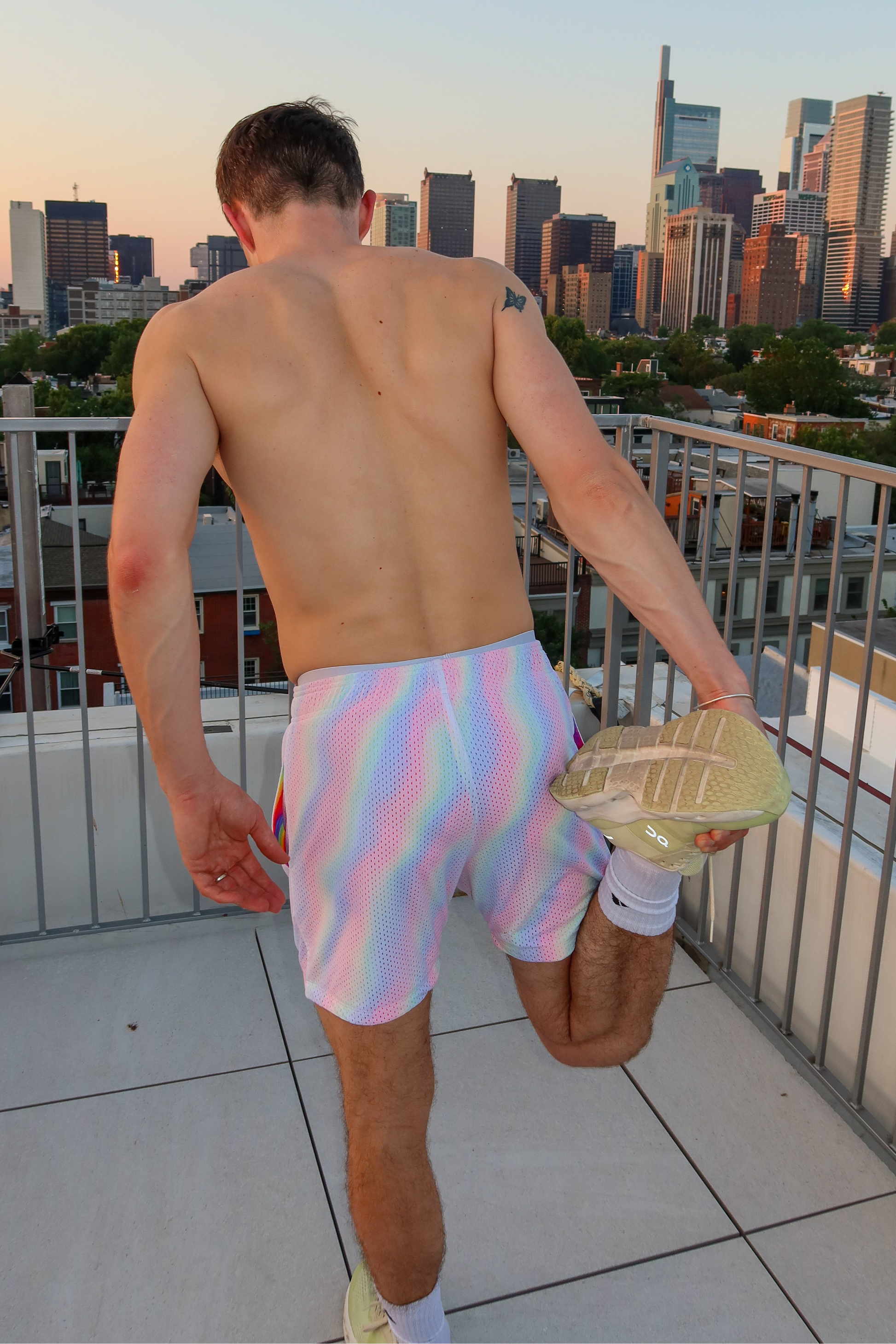 Man in tie-dye shorts standing on a rooftop with a city skyline in the background