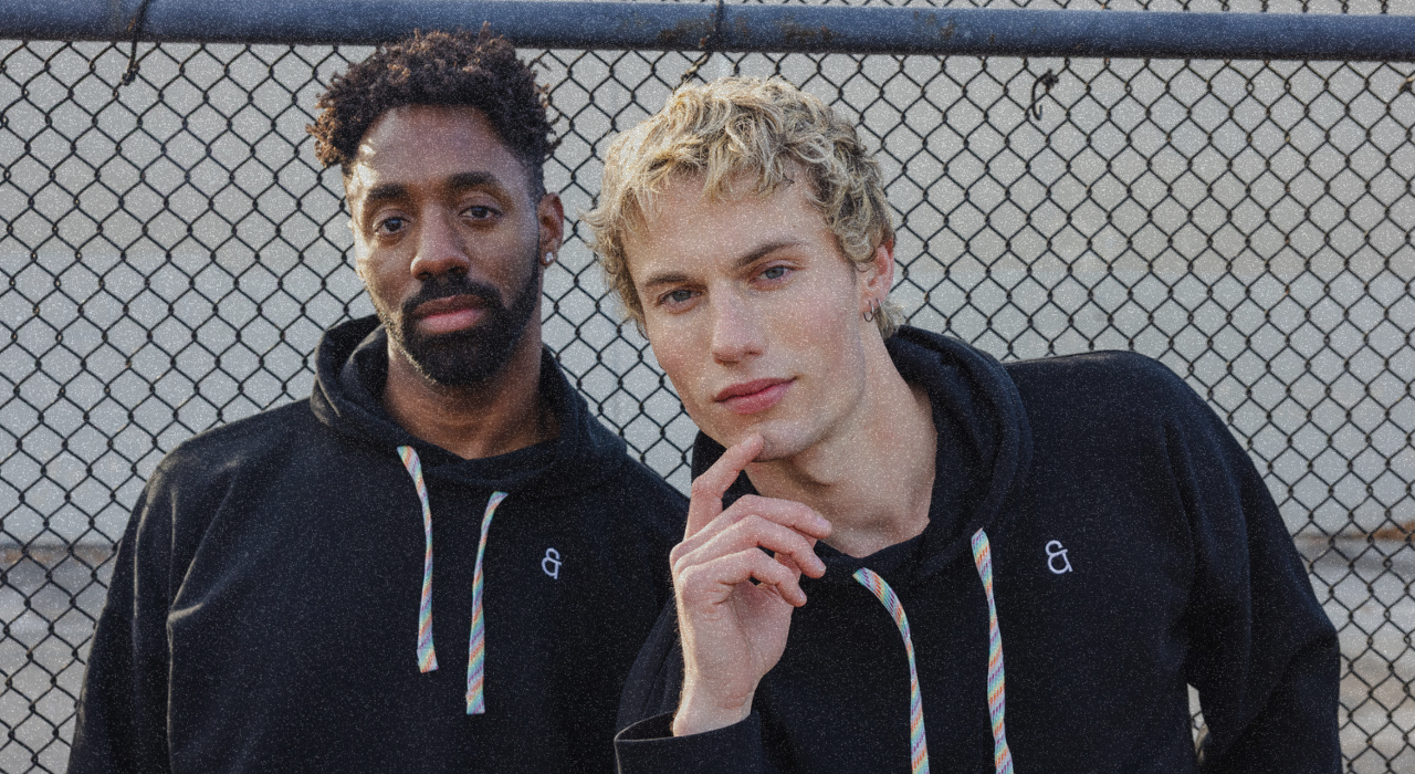 Two men wearing black hoodies standing in front of a chain-link fence.