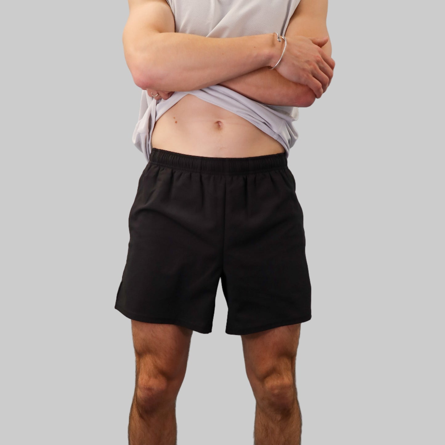 Person wearing a sleeveless shirt and black shorts standing against a light blue wall.