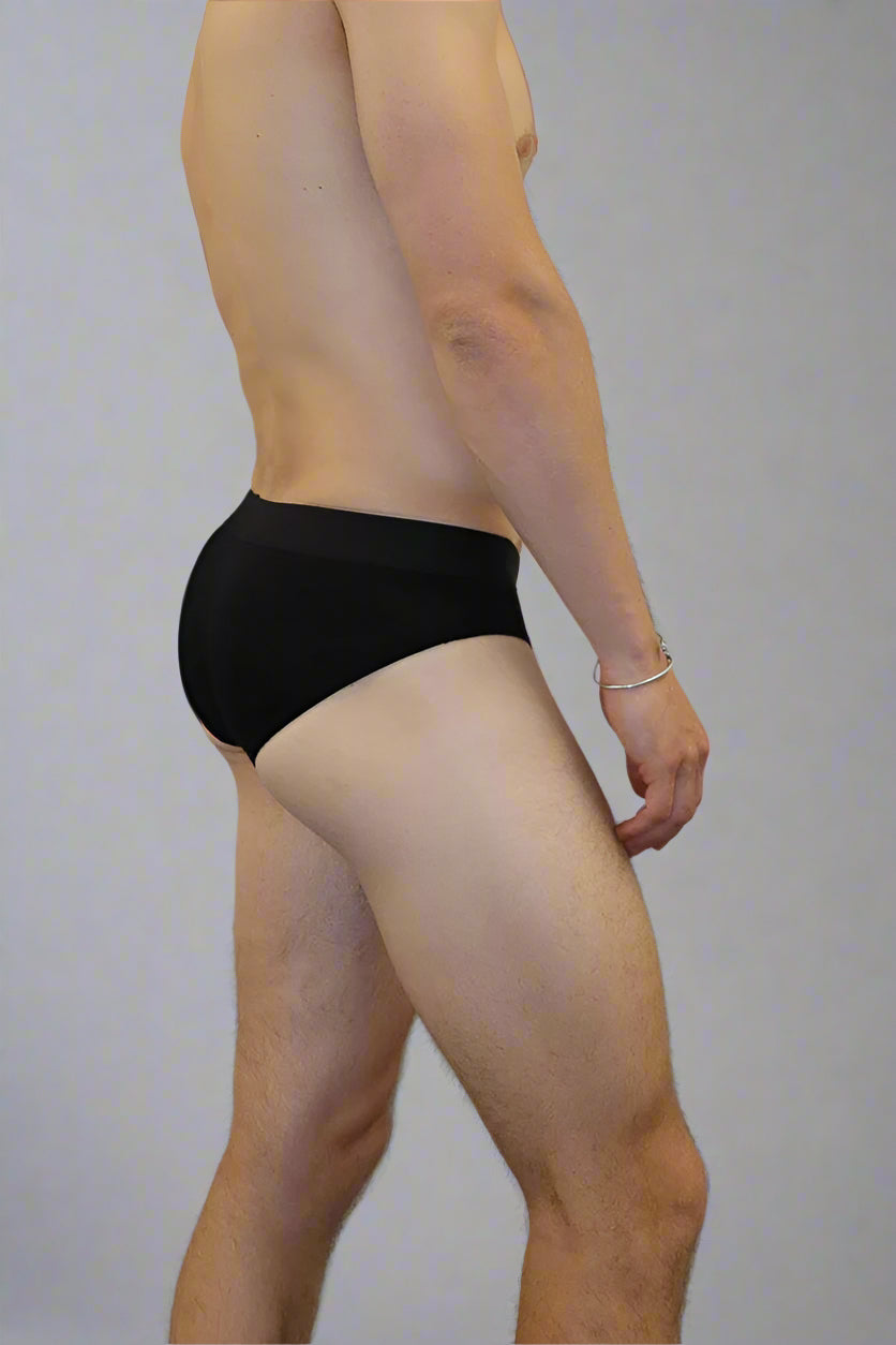 Man wearing black underwear against a plain wall