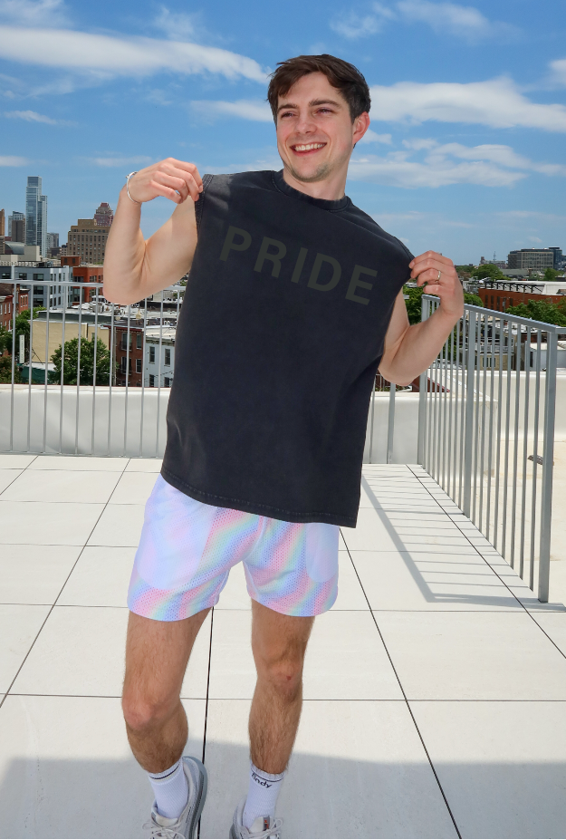 Person wearing a black 'PRIDE' t-shirt on a rooftop with a cityscape in the background